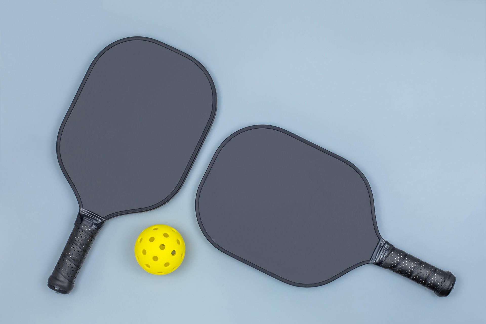 Two pickleball paddles and ball on light gray